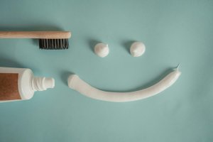 A creative arrangement of dental hygiene items forms a cheerful face on a light blue background. The 