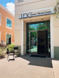 Exterior view of IDC San Bernardino office from a left angle with the door open, welcoming patients inside. There are 2 chairs outside for seating.